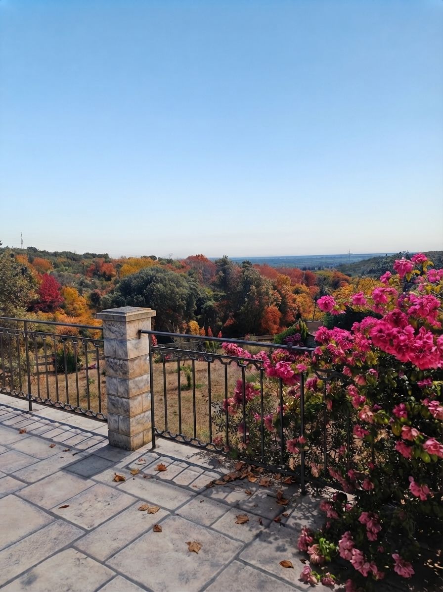 Un balcon doté d’un pilier en pierre, d’une balustrade en métal et offrant une vue sur un paysage arboré et fleuri.