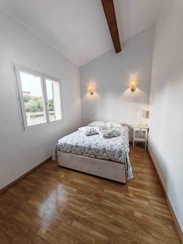 Une chambre à coucher comprenant un lit, un bureau, deux lampes fixées au mur et une fenêtre.