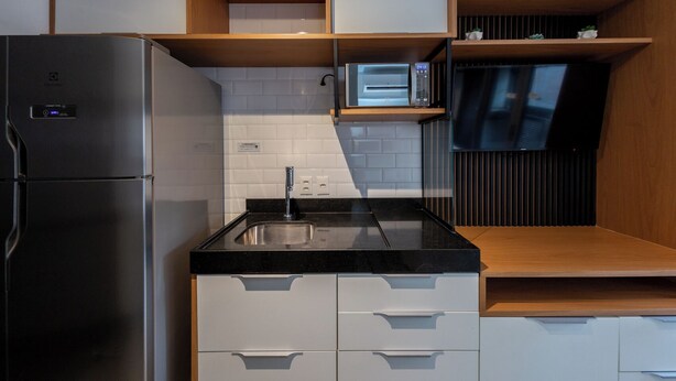 A compact kitchen with a stainless steel refrigerator, a microwave, and a sink. - Oscar by Bhomy (São Paulo)