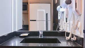 A modern bathroom with a black countertop, a glass sink, and a hairdryer mounted on the wall. - Oscar by Bhomy (São Paulo)
