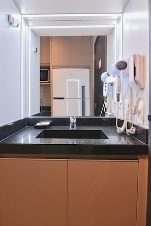 Ein modernes Badezimmer mit schwarzem Waschtisch, einem Glasbecken und einem an der Wand montierten Föhn.
