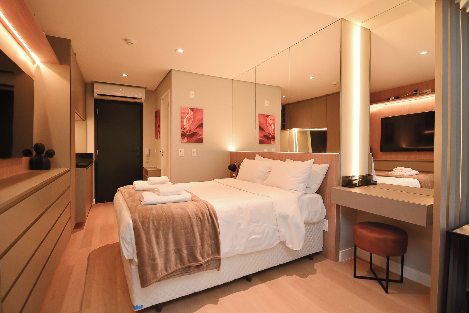 Quarto de hotel moderno com uma cama grande, mesa de cabeceira e televisão.