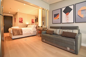 Ein Hotelzimmer mit Bett, Sofa und Schreibtisch. An der Wand befinden sich Bilder in Rahmen.
