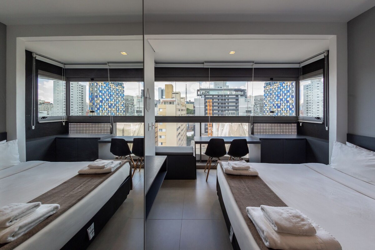 Ein modernes Hotelzimmer mit zwei Betten, einem Schreibtisch und Blick auf die Stadtlandschaft.