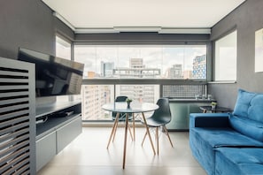 A modern living space with a television, a dining table with chairs, and a blue sofa. - Oscar by Bhomy (São Paulo)
