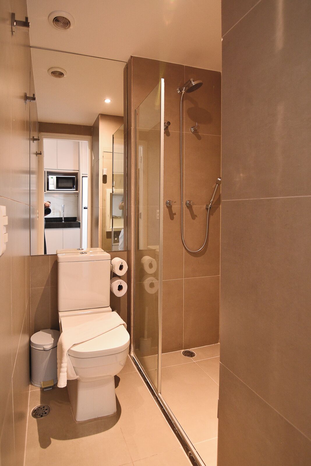 Een moderne badkamer met toilet, een douche met glazen wanden en een magnetron boven de wastafel.