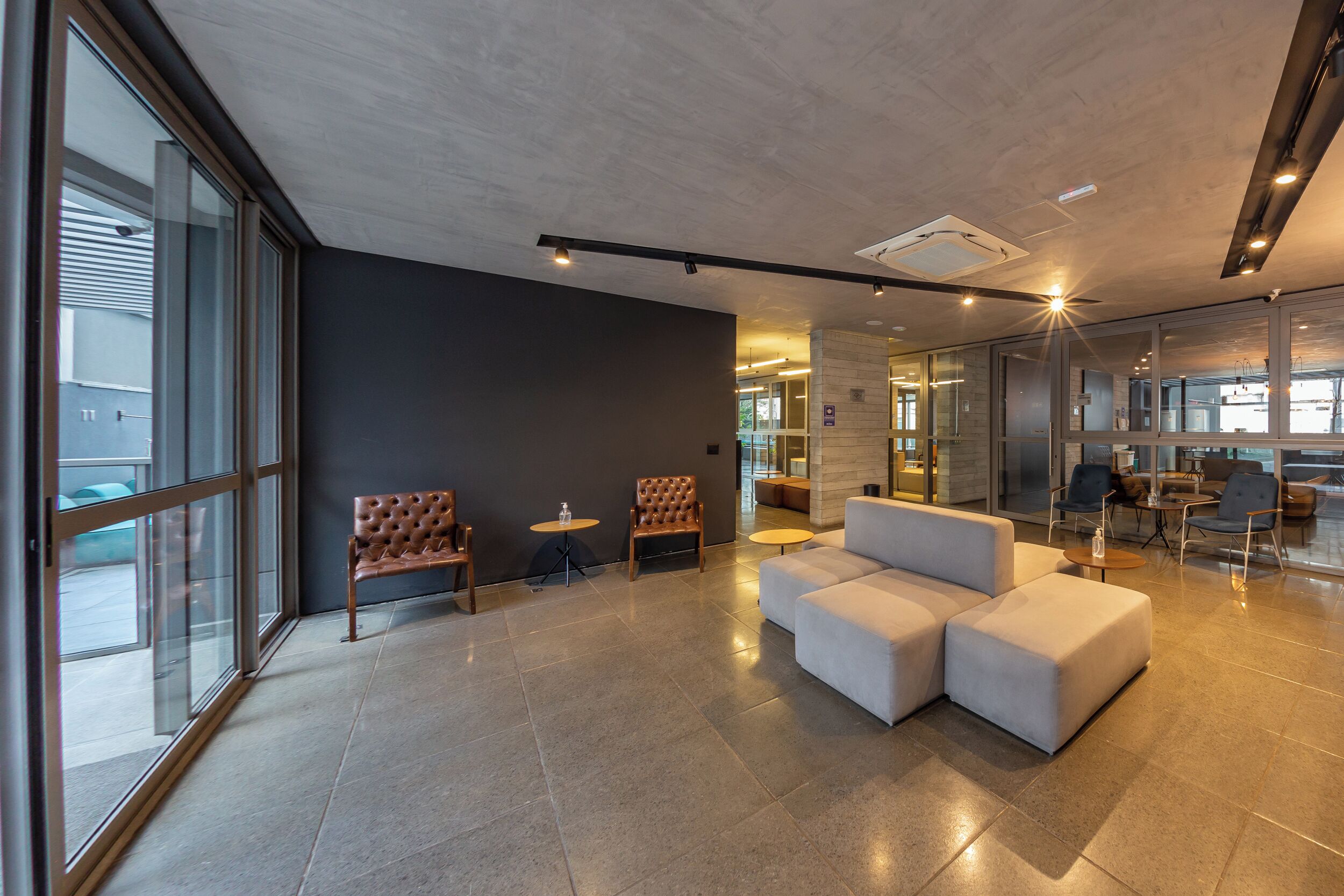 Um lobby moderno com assentos, uma parede de vidro e um teto com iluminação embutida.