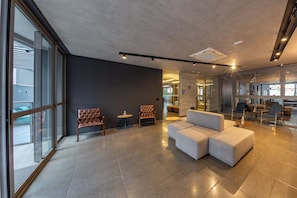 Um lobby moderno com assentos, uma parede de vidro e um teto com iluminação embutida.