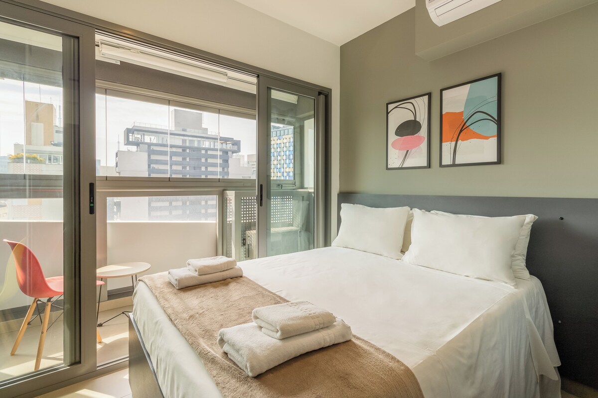 Ein Hotelzimmer mit Bett, Fenster, Sessel und zwei Bildern an der Wand.