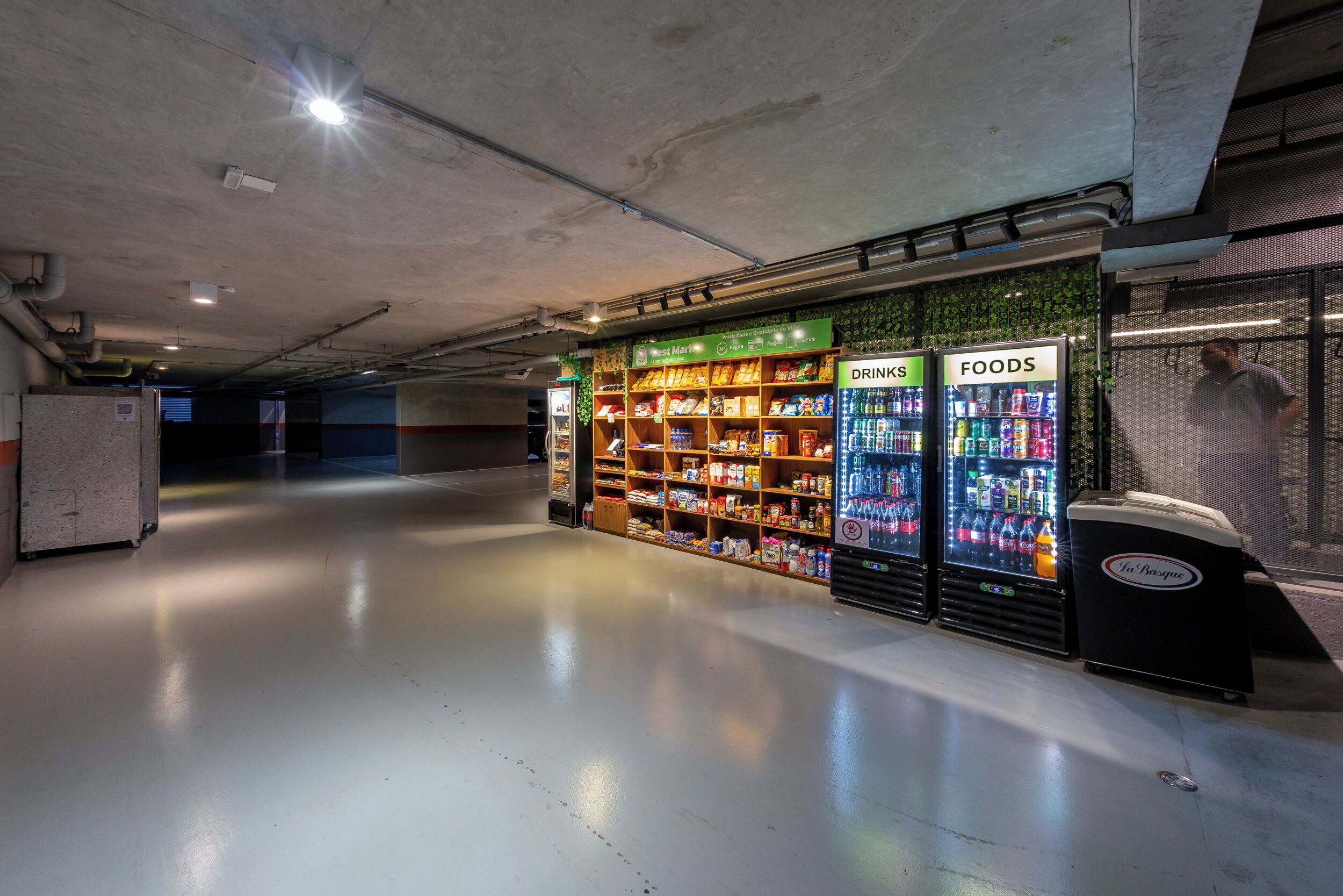 Um espaço interno limpo e bem iluminado, com máquinas de venda automática identificadas como 'BEBIDAS' e 'ALIMENTOS', abastecidas com diversas bebidas e lanches.