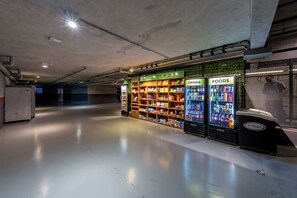 Um espaço interno limpo e bem iluminado, com máquinas de venda automática identificadas como 'BEBIDAS' e 'ALIMENTOS', abastecidas com diversas bebidas e lanches.