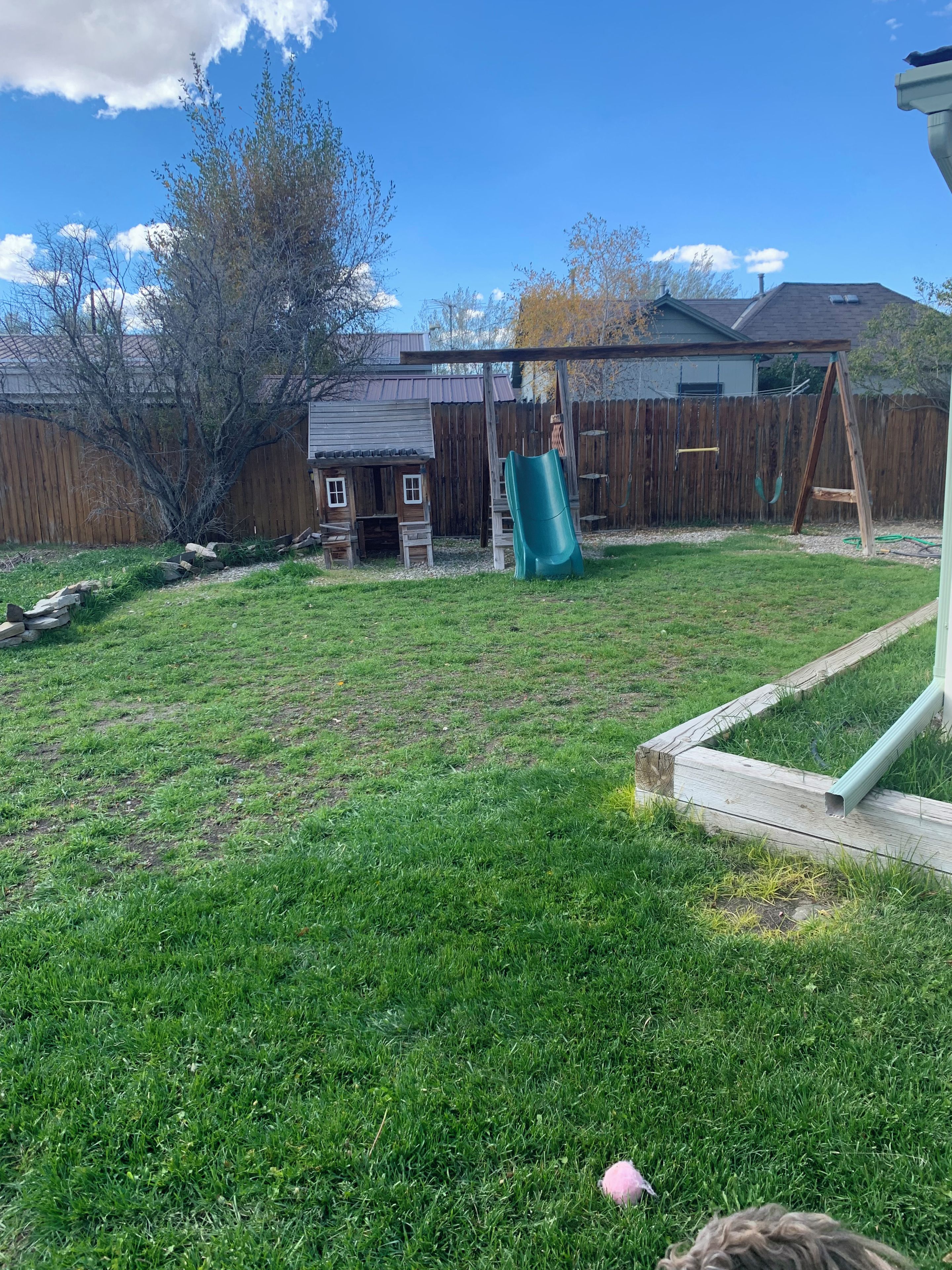 A backyard with a wooden playhouse, a slide, and a swing set.