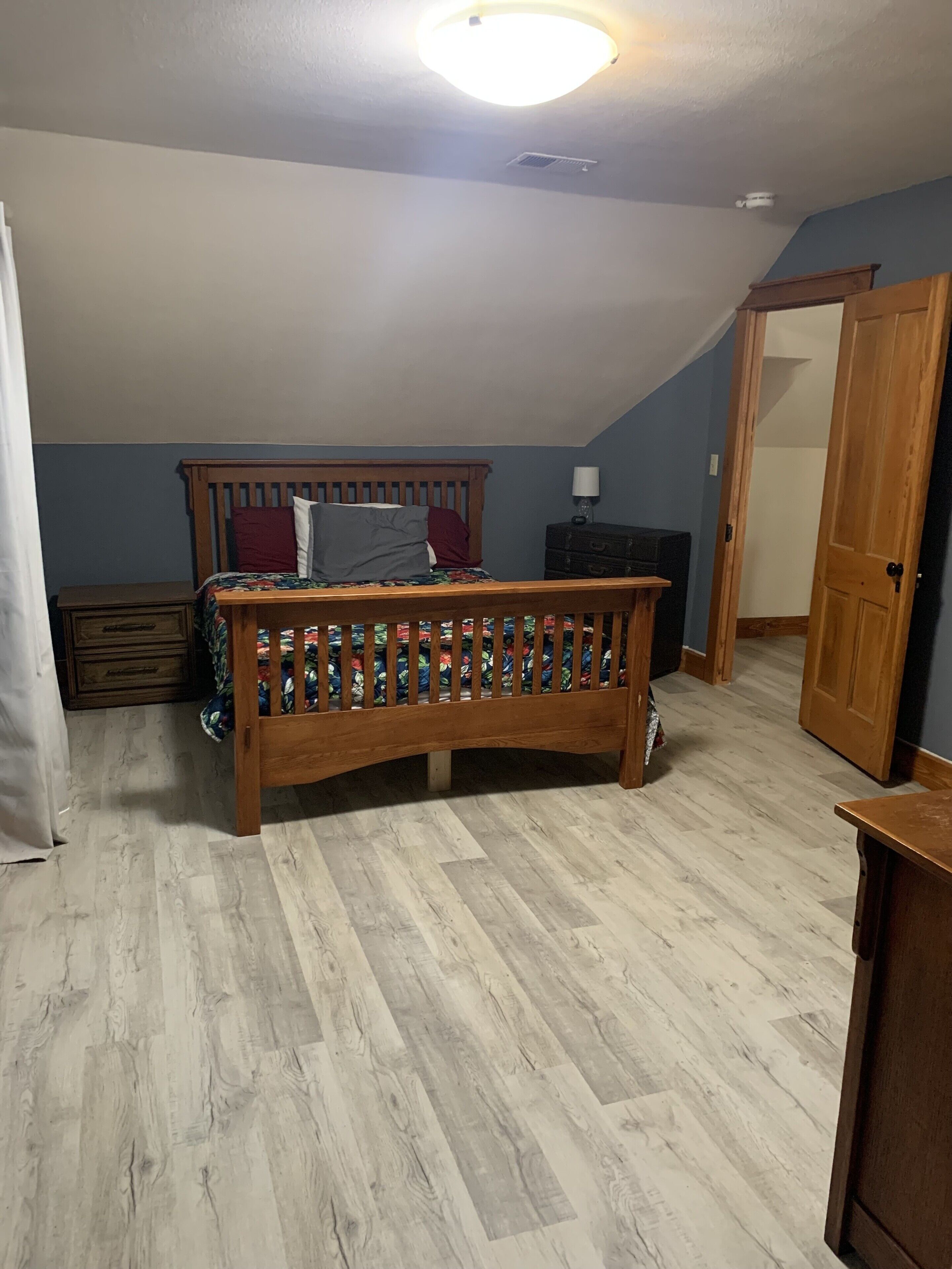 Una camera da letto con un letto in legno, un comodino, una cassettiera e una porta che dà su un'altra stanza.