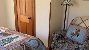 A bedroom with a wooden door, a patterned armchair, a quilted bedspread, and a wall-mounted lamp.