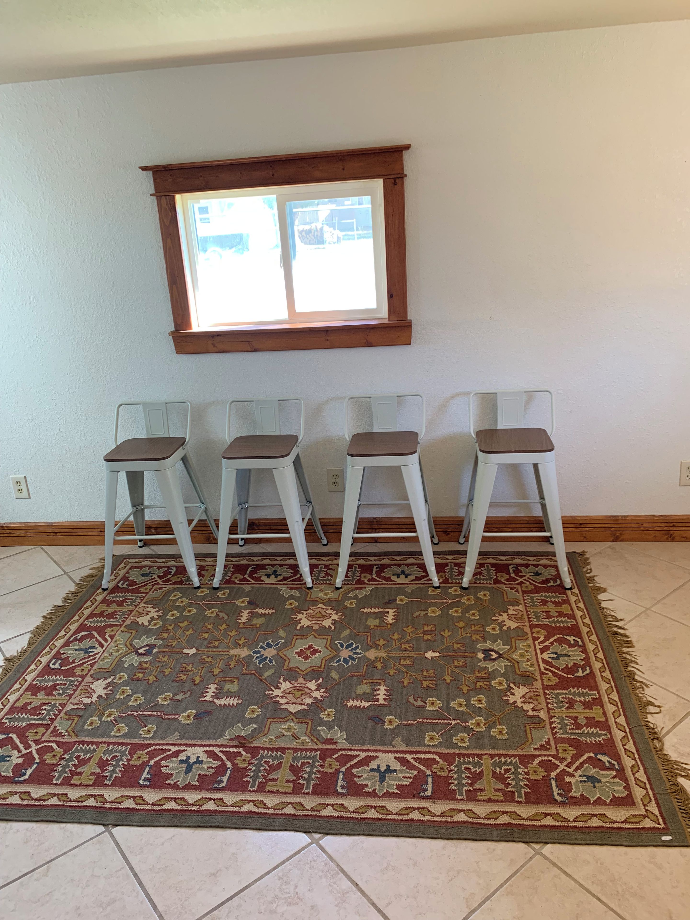 Ein Zimmer mit vier weißen Stühlen, die in einer Reihe angeordnet sind, einem gemusterten Teppich auf dem Boden und einem Fenster darüber.