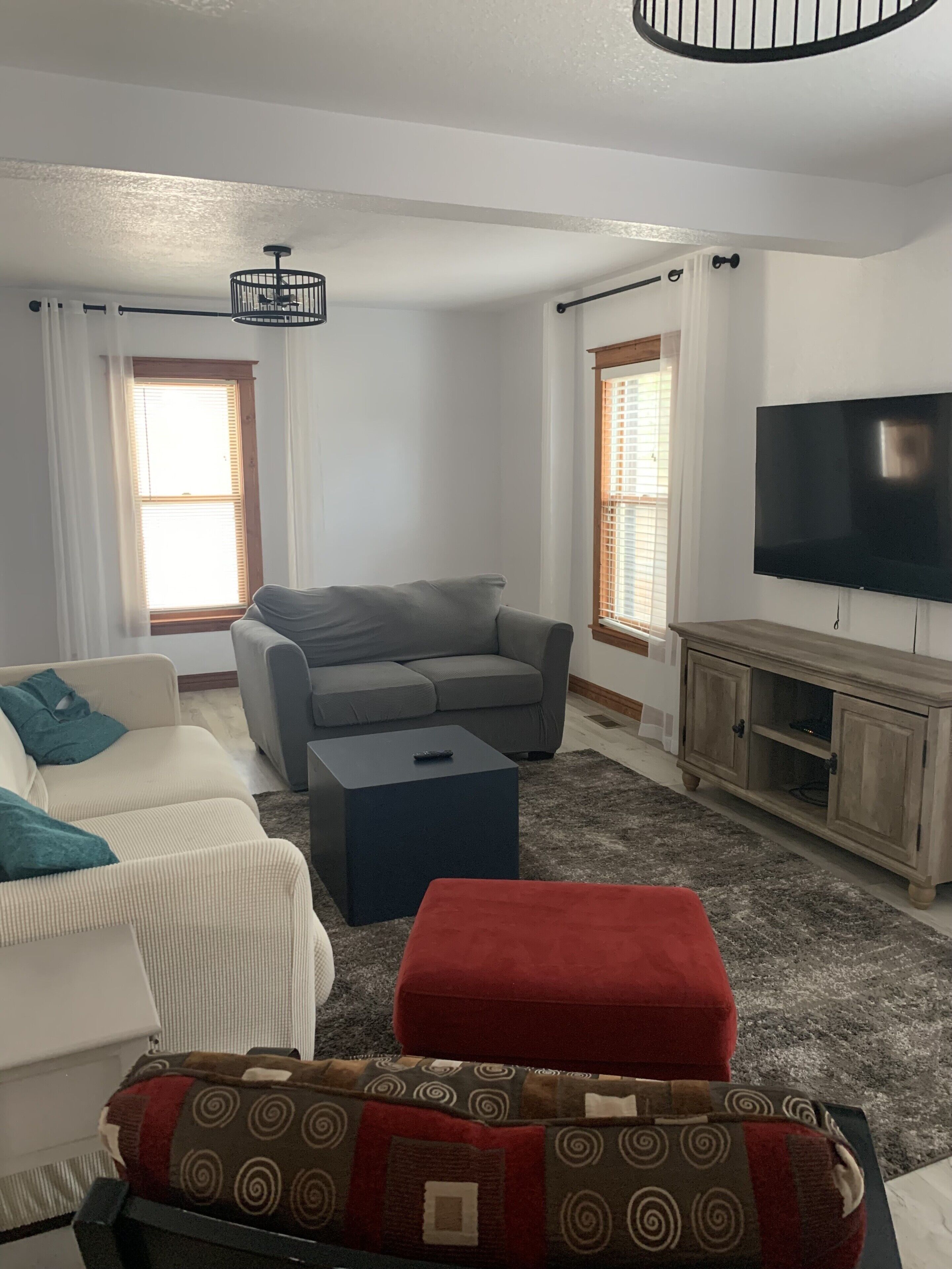 A living room with a grey sofa, a white sofa, a red ottoman, a black coffee table, and a television on a wooden cabinet.