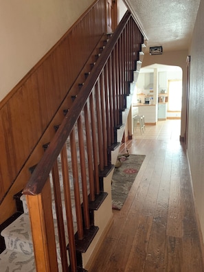 Una escalera de madera que lleva a una zona de cocina con una mesa y sillas.