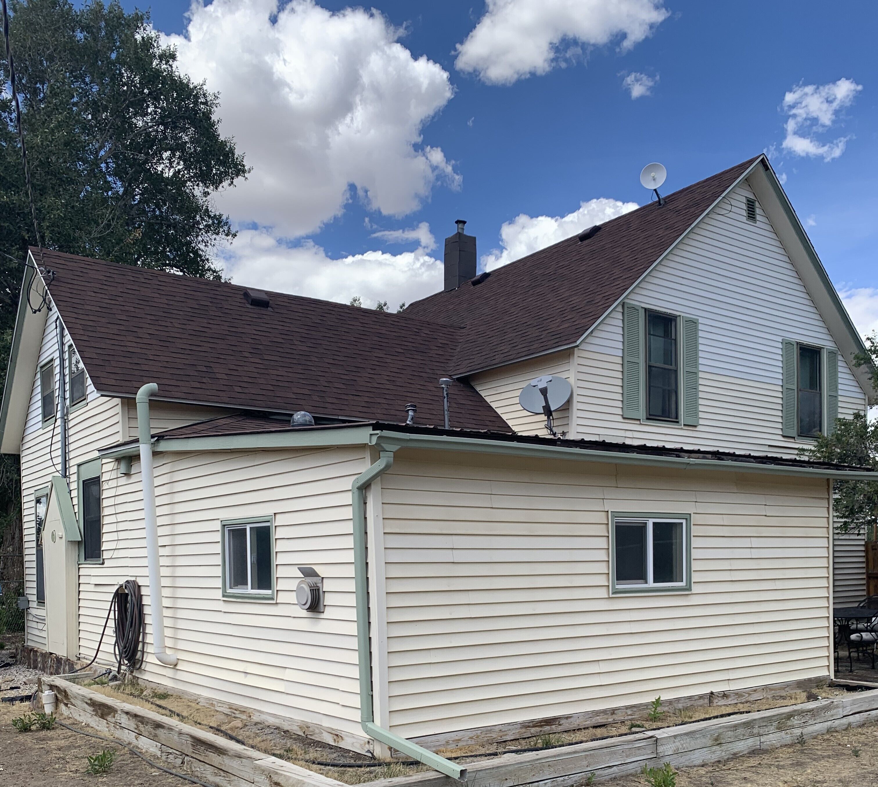 A two-story house with a brown roof, satellite dishes, and a visible chimney.