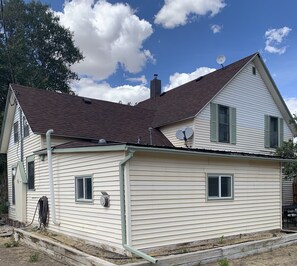 A two-story house with a brown roof, satellite dishes, and a visible chimney.