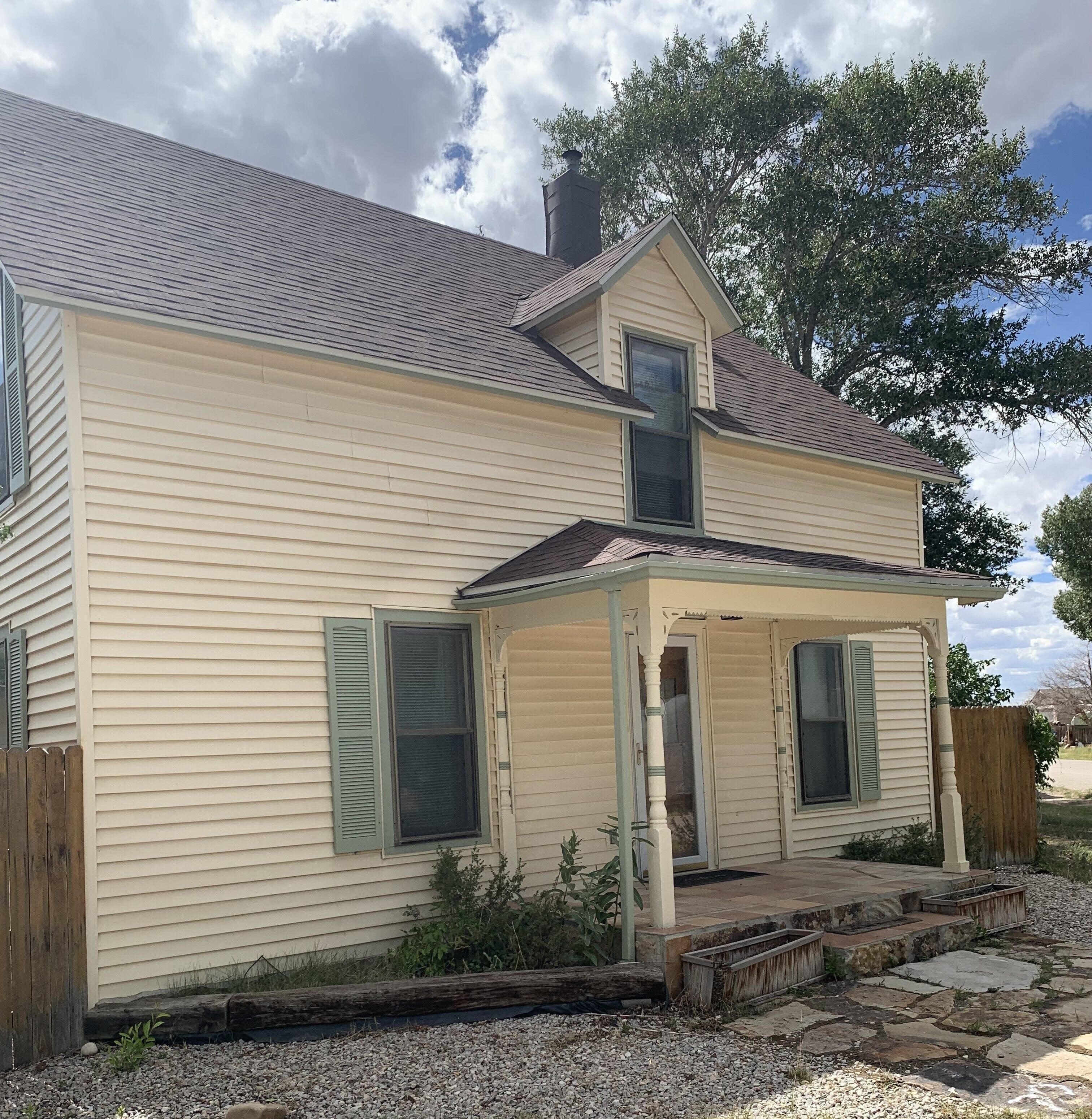 A two-story house with a porch, a chimney, and a wooden fence.