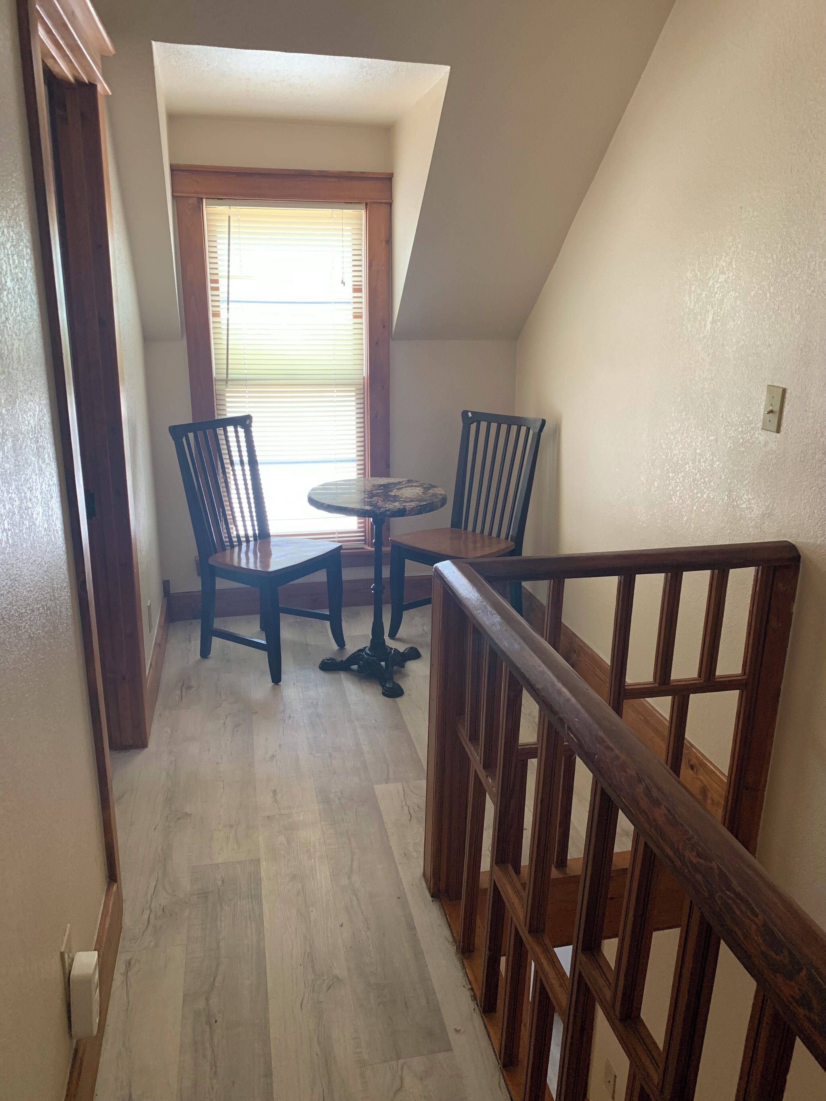 A staircase with wooden railings leading to a dining area with a round table and two chairs.