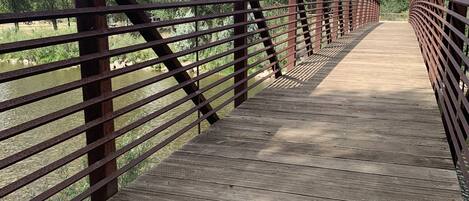 Een houten voetgangersbrug met metalen leuningen, die uitkomt op een natuurlandschap.