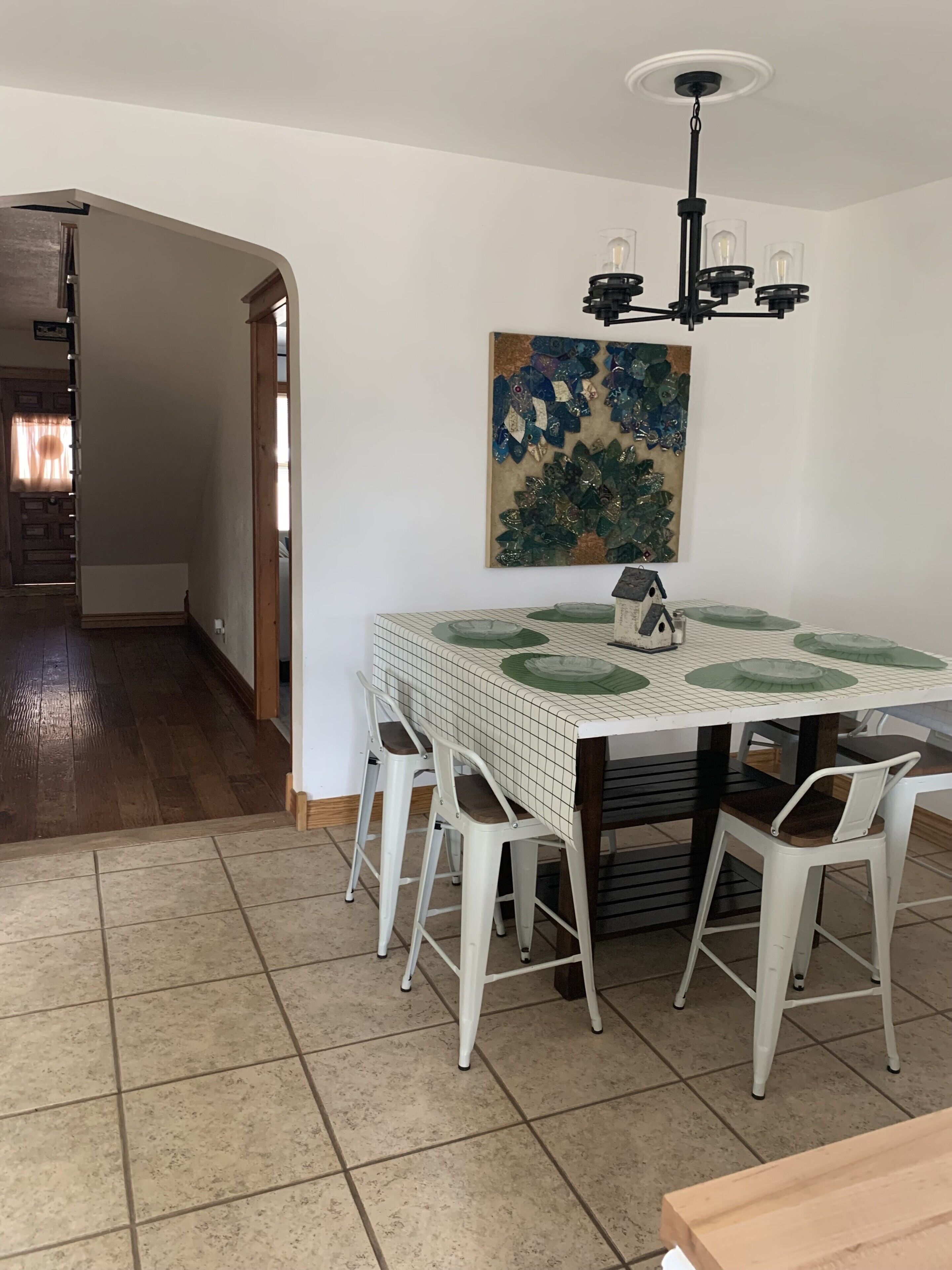 A dining area with a tiled table, white chairs, and a chandelier.