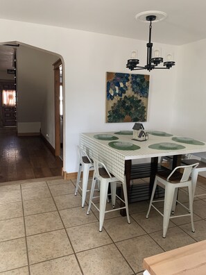 A dining area with a tiled table, white chairs, and a chandelier.