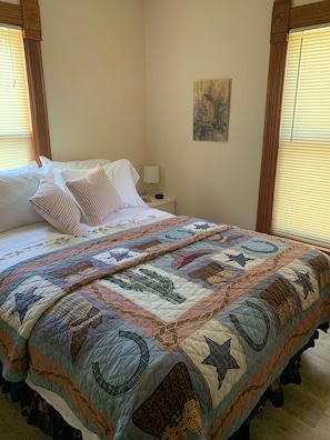 Una cama bien hecha con un edredón colorido, una lámpara de noche y un cuadro en la pared.