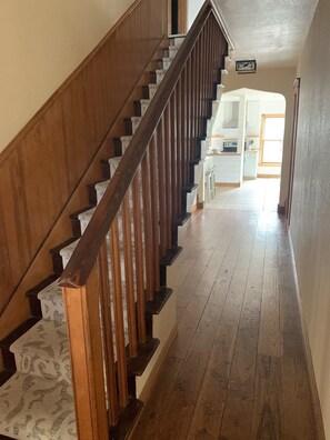 A wooden staircase leading to a kitchen area with white cabinets and a window.