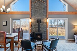 A cozy room with a fireplace, large windows, and a dining area. - The Northwood Nook on the Lake (Emily)