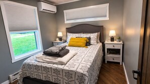 Een slaapkamer met een bed, twee nachtkastjes, een raam met jaloezieën en een airconditioning.
