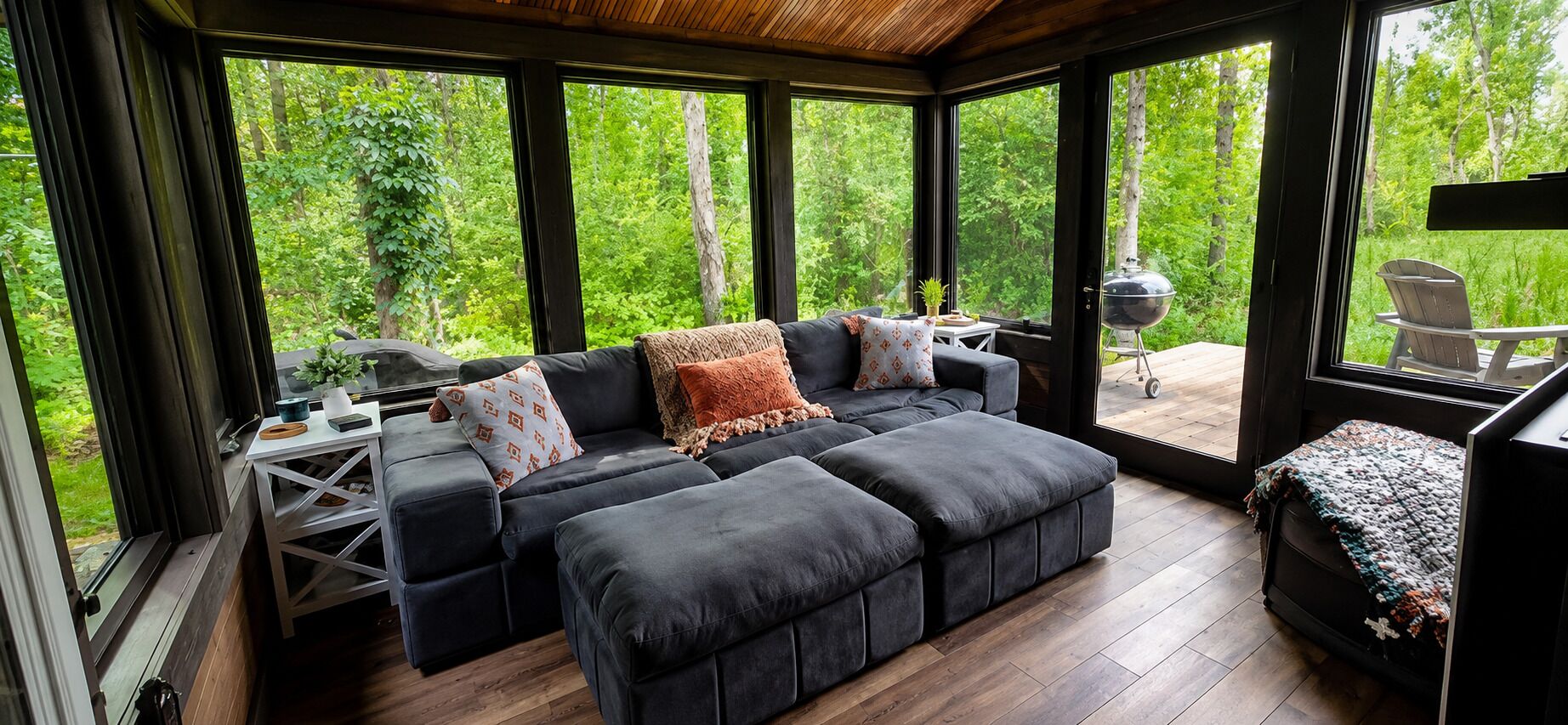 A modern living room with a sectional sofa, a small table, and a grill outside.