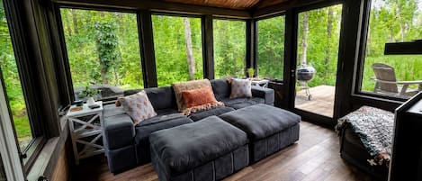 A modern living room with a sectional sofa, a small table, and a grill outside.