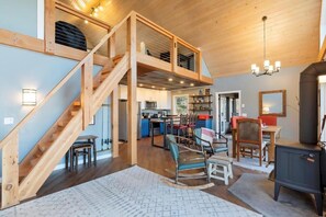A spacious loft-style living area with a wooden staircase, a dining area, and a kitchen. - The Northwood Nook on the Lake (Emily)