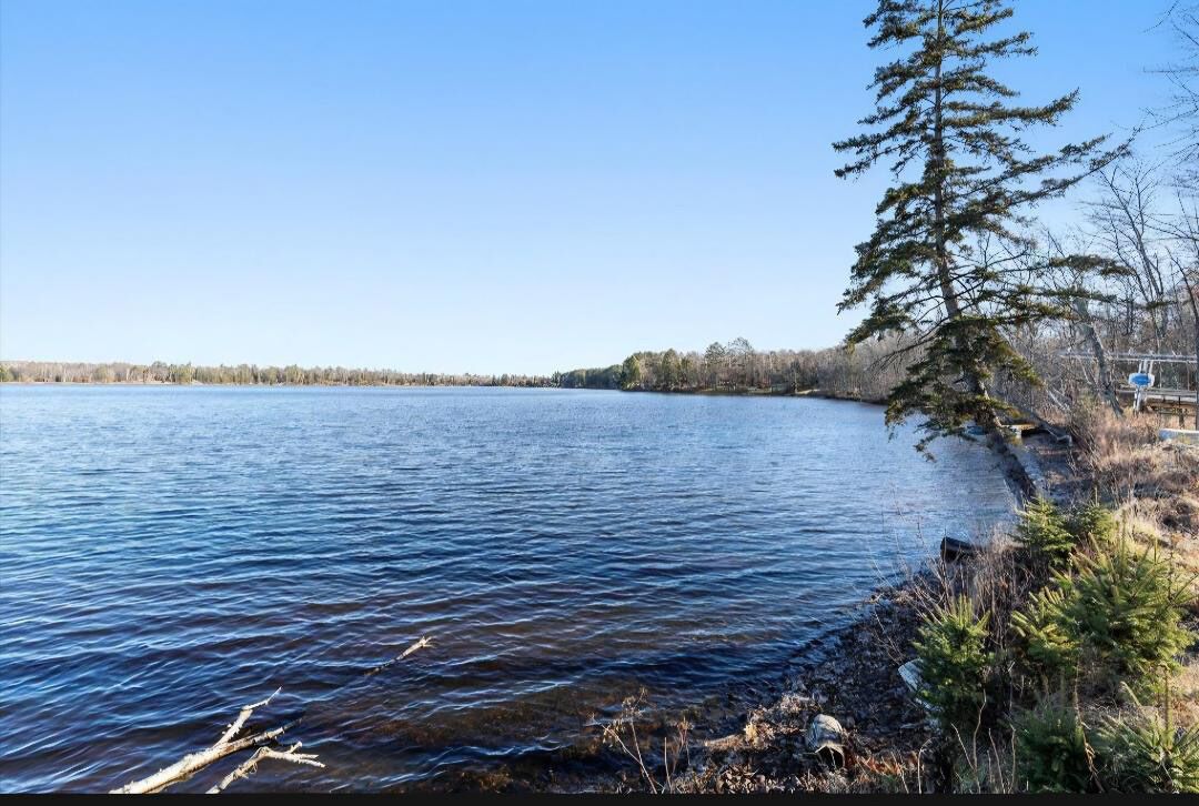 A calm lake with a clear sky, surrounded by trees and a rocky shoreline.