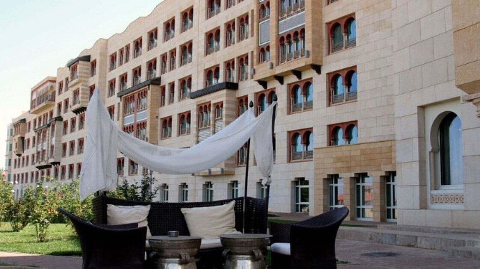 A hotel with multiple balconies, outdoor seating with white drapes, and a well-maintained garden area.