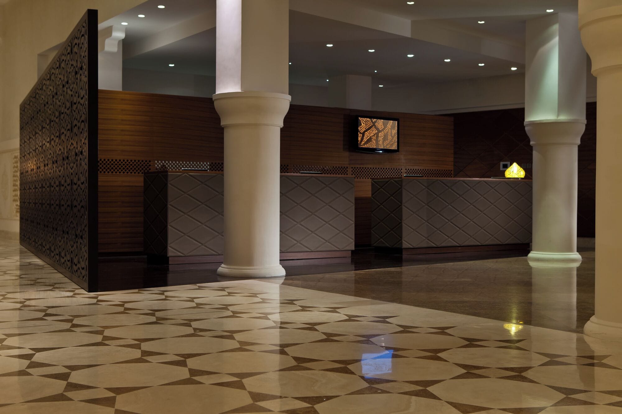 A reception area with a patterned floor, a reception desk, and a wall-mounted screen.