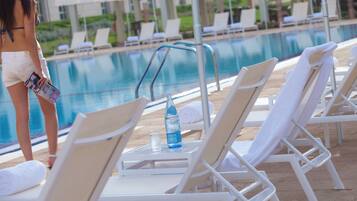 A poolside area with lounge chairs, a pool, and a person holding a magazine.