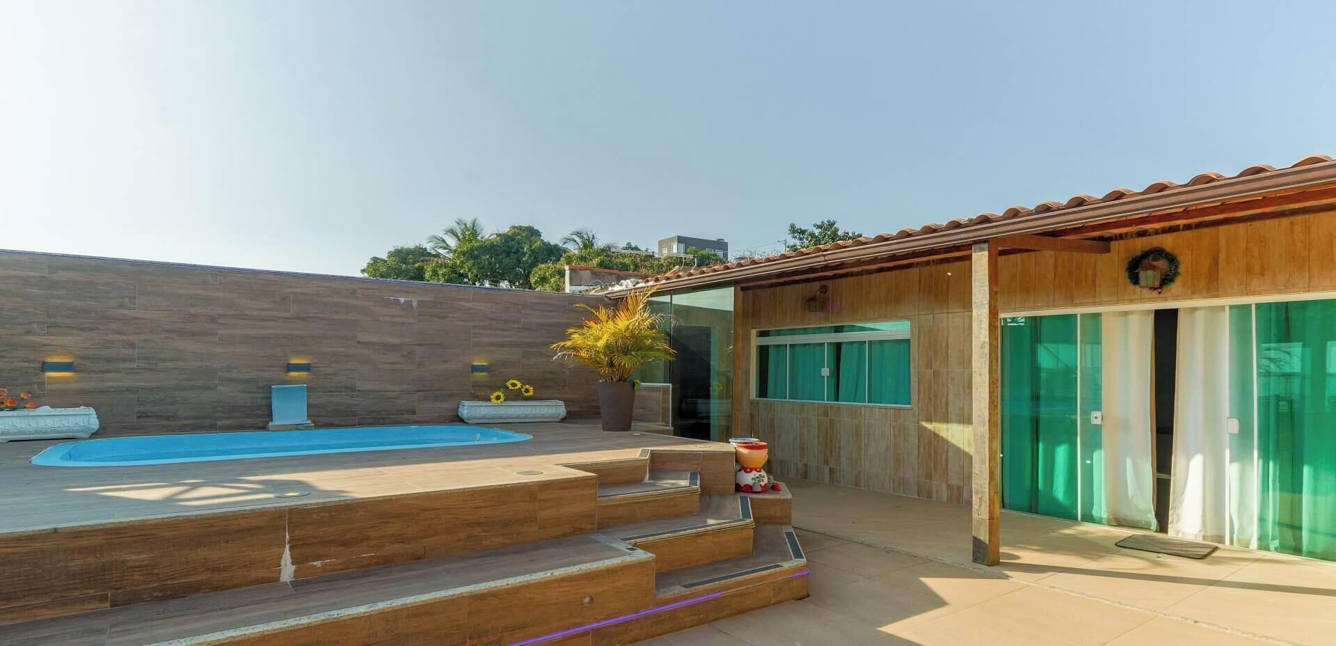 A modern outdoor pool area with a wooden deck, a small waterfall feature, and a glass door entrance.