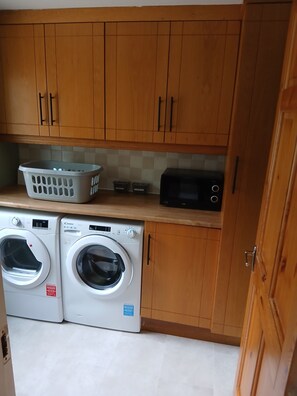 A laundry area with two washing machines, a basket, and a microwave.