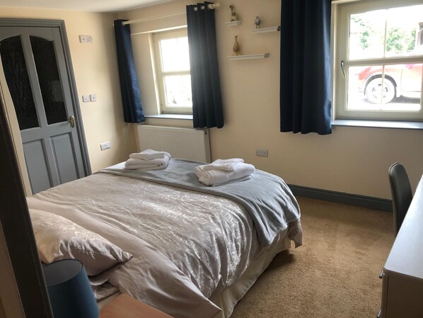 A hotel room with a bed, a desk, a chair, a radiator, and a window with curtains.