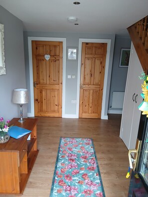 A hallway with wooden doors, a blue floral rug, a desk with a lamp, and a vase with flowers.