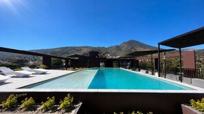 A rooftop swimming pool with lounge chairs, surrounded by a modern architectural structure and a mountainous backdrop. - Brand New Apt Avitat Unique: Beauty Modern Cozy Great View. (San salvador)