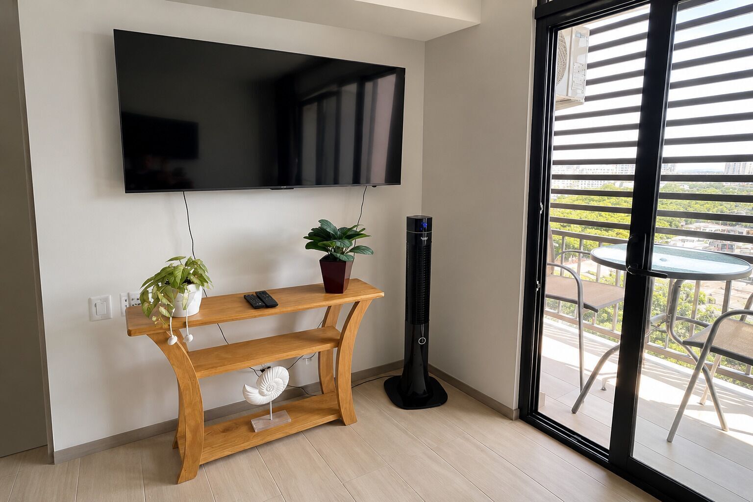 Un salon moderne avec un téléviseur à écran plat fixé au mur, une console en bois sur laquelle est posée une plante en pot, un radiateur mobile et une vue sur l’extérieur grâce à une porte-fenêtre coulissante.