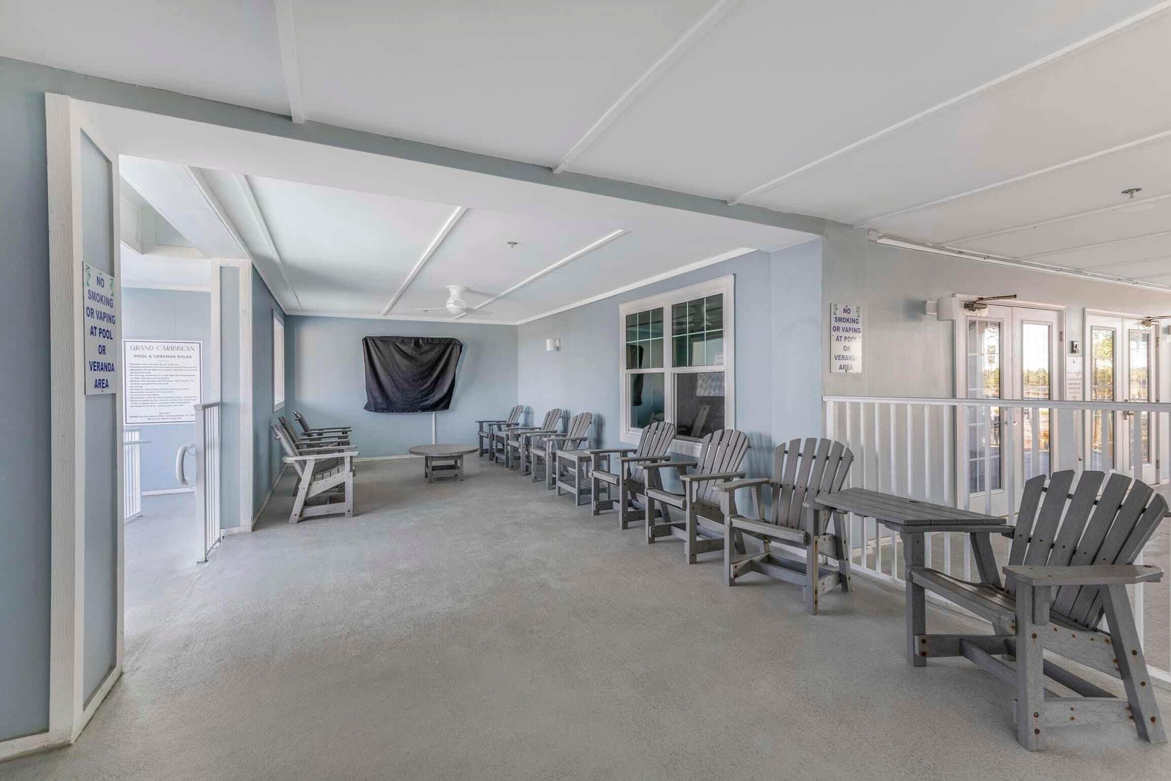 A room with a long table and several Adirondack chairs arranged for dining. There are signs indicating no smoking and no vaping at the pool.