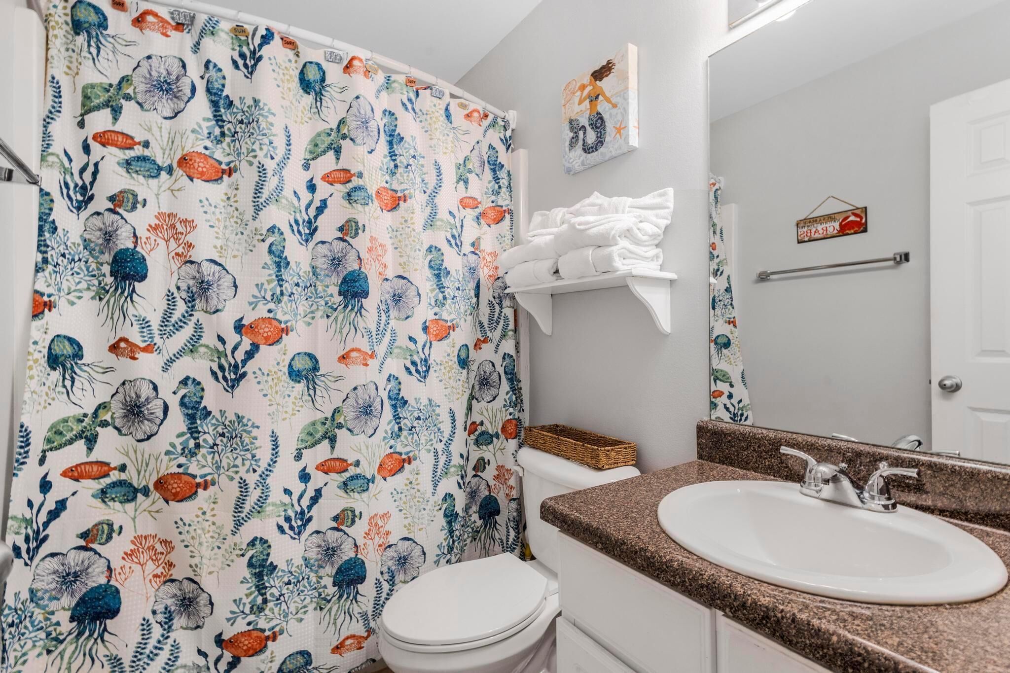 A bathroom with a shower curtain featuring a marine life pattern, a white toilet, a sink with a granite countertop, and a mirror above the sink.