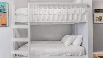 Una cama individual con ropa de cama y almohadas blancas, un cuadro enmarcado en la pared y una pequeña estantería.