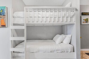 A bunk bed with white bedding and pillows, a framed picture on the wall, and a small shelf unit. - Grand Caribbean 423 (Orange Beach)