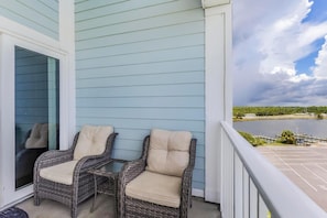 A balcony with two wicker chairs and a small table, overlooking a body of water and a distant shoreline. - Grand Caribbean 423 (Orange Beach)
